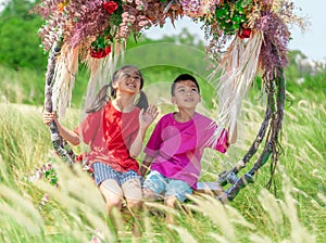 Two siblings children is swinging on a flower swing in a nature field for relaxation and childhood hapiness concept