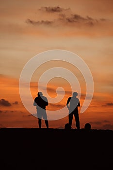 Two silhouetted figures standing against orange sunset skies