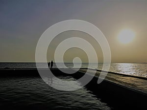 Two silhouettes accompany the sun on the pier