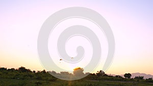 Two silhouettes of paramotors are flying