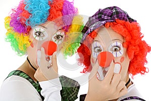 Two silly women as clowns made up in costume for carnival pinch their red noses