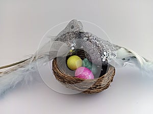 Two silver birds perched on a nest with eggs on a white background