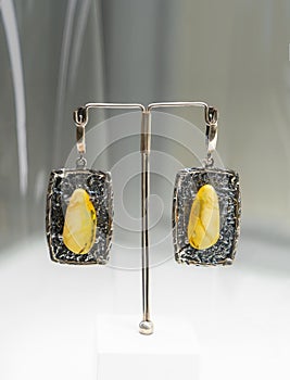 Two silver earrings with amber on a glass shelf