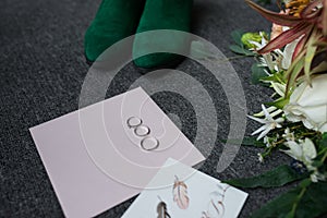 Two silver wedding rings and an engagement ring on the envelope. Green bridal shoes, a part of wedding bouquet and a wedding compl