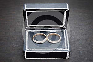 Two silver wedding rings in an open black velvet ring box on a dark surface