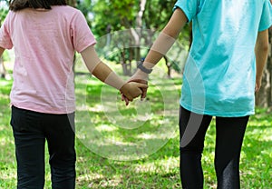 Two sister holding hands in the park in warm spring day. Happy friendship family concept