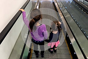 Two sister holds hands on moving walkway