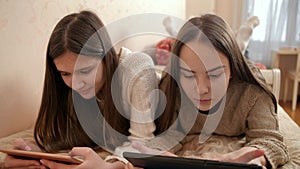 Two sister using tablets on bed. Teenagers studying and using modern gadgets at home