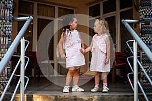 Two sisters blonde and brunette baby girls in the same dresses, holding hands