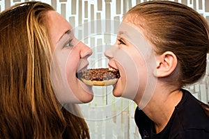 two sisters crunching in delicious chocolate donuts