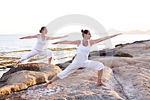 Two sisters are doing yoga exercises at the seashore of Mediterranean sea