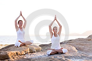 Two sisters are doing yoga exercises at the seashore of Mediterranean sea