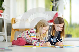 Two sisters drawing with colorful pencils at home. Creative kids doing crafts together. Education and distance learning for kids.