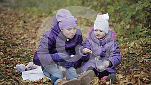 Two sisters drink cocoa with marshmallows in the autumn park