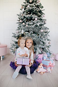 Two sisters at home with Christmas tree and presents. Happy children girls with Christmas gift boxes and decorations.