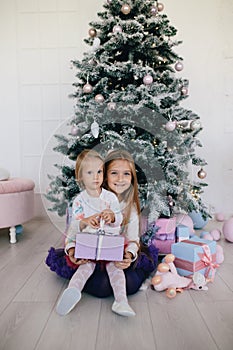 Two sisters at home with Christmas tree and presents. Happy children girls with Christmas gift boxes and decorations.