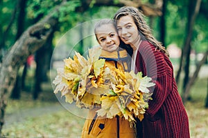 Two sisters hug, with a bunch of leaves in the park.