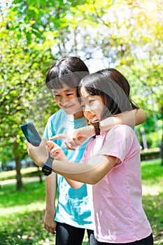 Two sisters hugging while using mobile phone in the park. Happy family concept