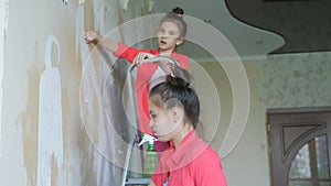 Two sisters with interest rips the old Wallpaper from the wall helping her parents to make repairs.