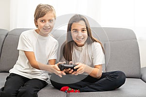 Two sisters kids playing video games at home together. Happy childeren, carefree childhood concept