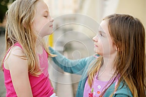 Two sisters laughing and hugging on warm and sunny summer day in a city. Cute siblings having a good time together