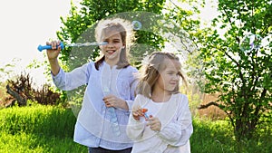 Two sisters little girls inflate soap bubbles on a picnic