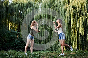 Two sisters, making blowing soap bubbles in park in summer. Young pretty girls, wearing jeans shorts and green beige tops, having