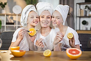 Two sisters with mother holding slices of citrus in hands