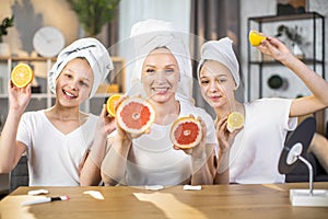 Two sisters with mother holding slices of citrus in hands