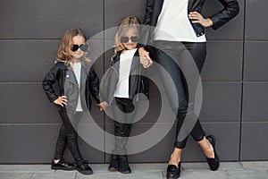 Two sisters with mother in same outfits: white t-shirts, leather black jackets and leggings, sunglasses hearts.