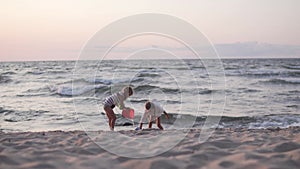 Two sisters play beach toys by the sea at sunset in the summer