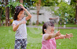 Two sisters playing bubbles at a park with green grass, laughing and smiling