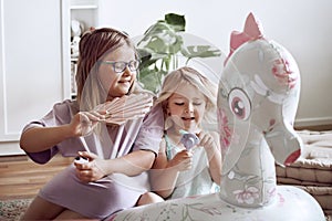 Two sisters playing with fans and pool cruiser in their room during summer heat wave. Siblings