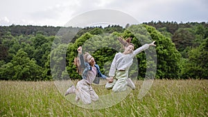 Two sisters playing at meadow in grass, having fun, running and jumping. Sisterly love and siblings relationship concept