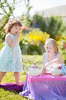 Two sisters playing tea party outdoors.