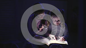 two sisters reading a book with a flashlight in a dark room at night