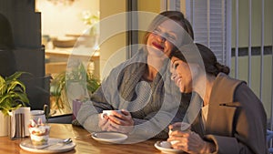 Two sisters relaxing in cafe, drinking hot coffee and chatting, having good time