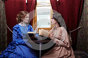 Two sisters in retro dress reading books in train compartment