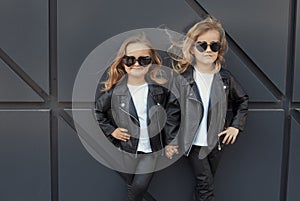 Two sisters in same outfits: white t-shirts, leather black jackets and leggings, sunglasses hearts.