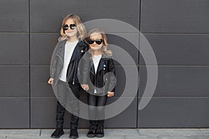 Two sisters in same outfits: white t-shirts, leather black jackets and leggings, sunglasses hearts.