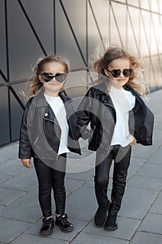 Two sisters in same outfits: white t-shirts, leather black jackets and leggings, sunglasses hearts.