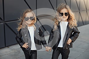 Two sisters in same outfits: white t-shirts, leather black jackets and leggings, sunglasses hearts.