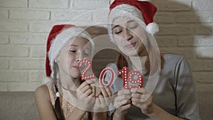 Two sisters in Santa`s hats are holding red numbers 2019 in their hands, playing with them, dancing and smiling sitting