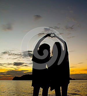 Two sisters silhouette making heart symbol