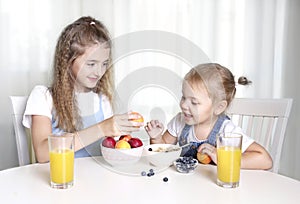 Two sisters sitting at kitchen table eating fruits.Healthy nutrition concept.Vitamin food.Children have a lunch.Frendship photo