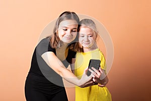 Two sisters take a selfie on a smartphone, on a light orange background