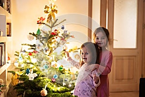 Two sisters together near Christmas tree at evening home