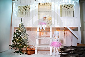 Two sisters twins in the costumes of dog poodles for the New Year. Girls playing on the porch of a white wooden house decorated wi