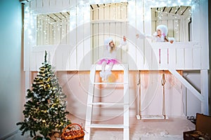 Two sisters twins in the costumes of dog poodles for the New Year. Girls playing on the porch of a white wooden house decorated wi