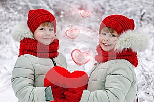 Two sisters twins are holding together a plushy heart. photo